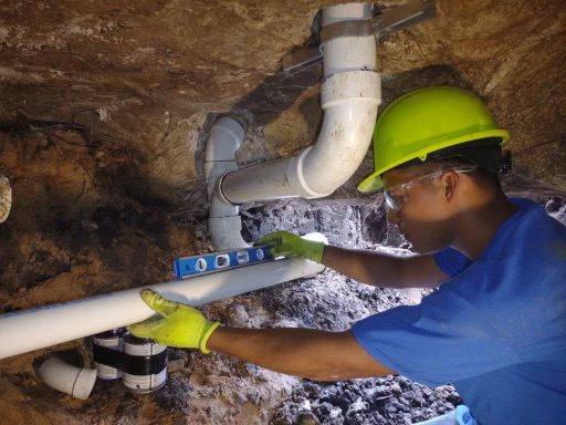a man in blue shirt and yellow helmet working on pipes