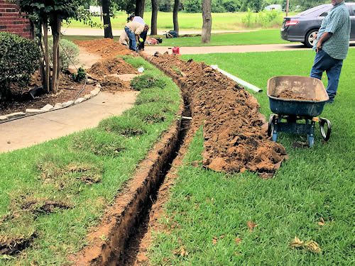 two men are digging in the grass with a wheelbarrow