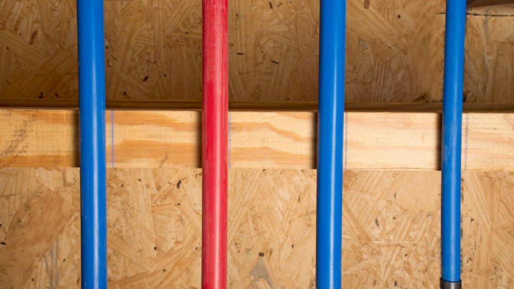 three red and blue baseball bats lined up against a wooden wall